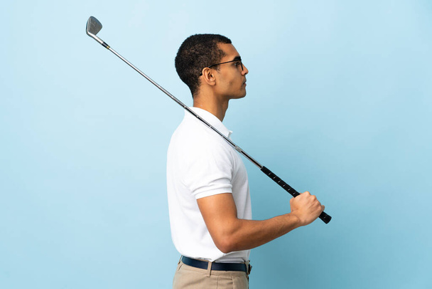 Hombre afroamericano sobre fondo azul aislado jugando golf en posición lateral - Foto, imagen