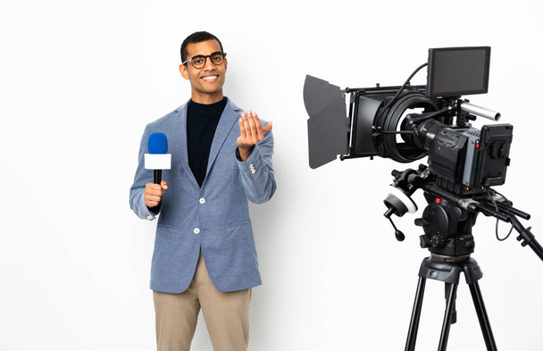 Δημοσιογράφος Αφροαμερικανός που κρατάει μικρόφωνο και μεταδίδει ειδήσεις σε απομονωμένο λευκό φόντο καλώντας τον να έρθει με το χέρι. Χαίρομαι που ήρθες. - Φωτογραφία, εικόνα