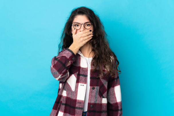 Adolescente rusa chica aislada sobre fondo azul cubriendo la boca con la mano - Foto, Imagen