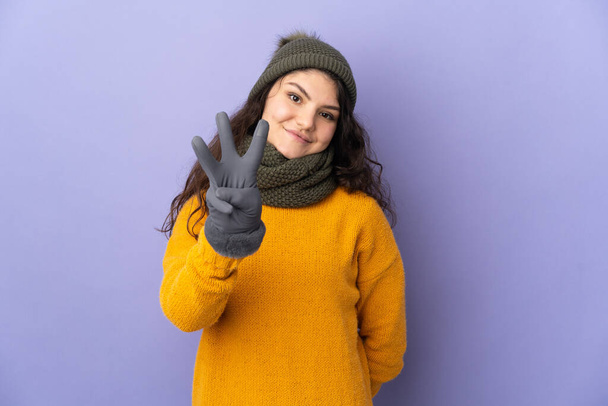 Adolescente russe fille avec chapeau d'hiver isolé sur fond violet heureux et comptant trois avec des doigts - Photo, image