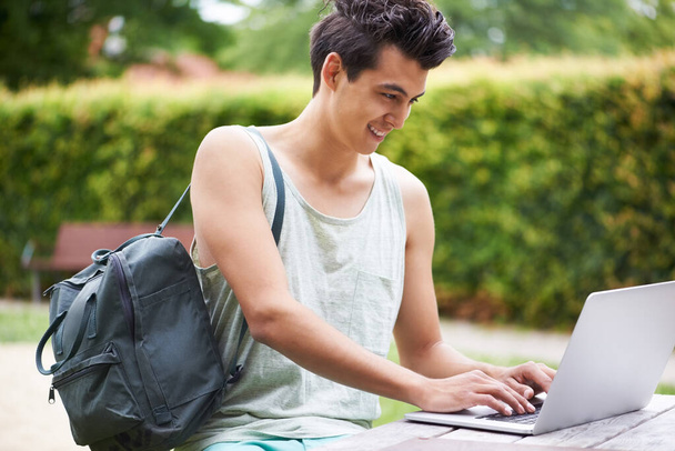 Redes en cualquier lugar y en cualquier momento. Un joven guapo escribiendo en su portátil mientras está sentado en el parque. - Foto, imagen