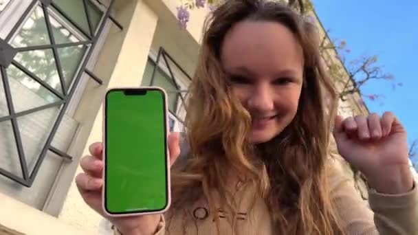 Gevşek saçlı, kahverengi saçlı genç kız, yeşil perdenin arka planında telefonla dans ediyor. - Video, Çekim