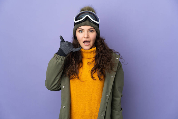 Tiener Russisch meisje met snowboardbril geïsoleerd op paarse achtergrond maken telefoon gebaar. Bel me terug. - Foto, afbeelding