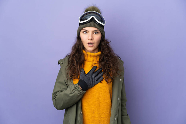 Adolescente rusa con gafas de snowboard aisladas sobre fondo púrpura sorprendida y sorprendida mientras mira a la derecha - Foto, imagen