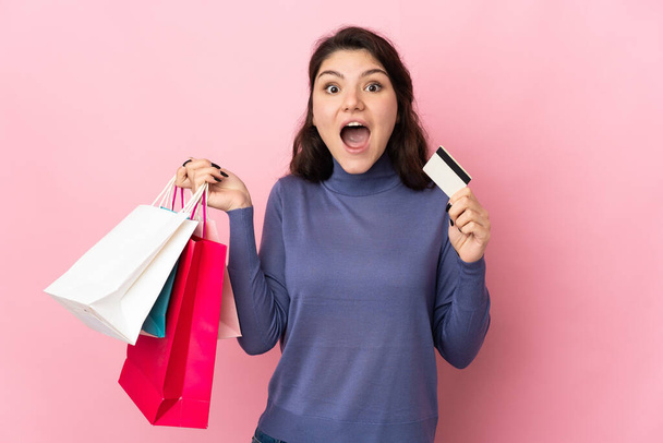 Teenager Russian girl isolated on pink background holding shopping bags and surprised - Foto, Imagem