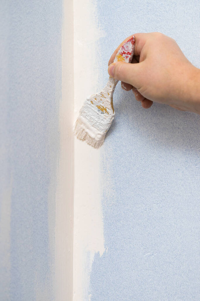 Person appplying white paint on blue wall using brush. Home renovation concept. - Photo, image