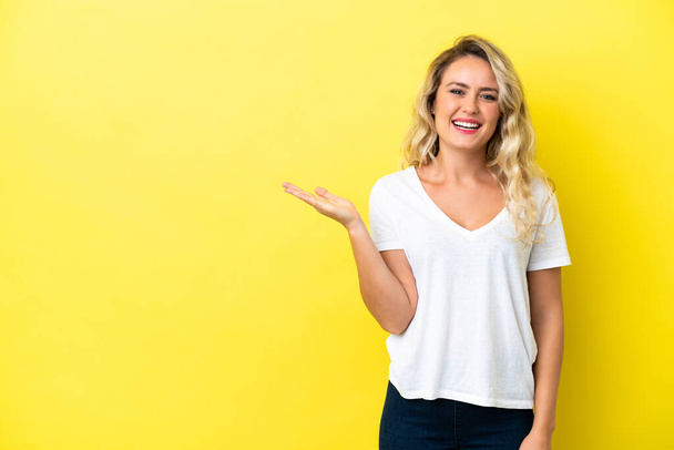 Young Brazilian woman isolated on yellow background holding copyspace imaginary on the palm to insert an ad - Photo, Image