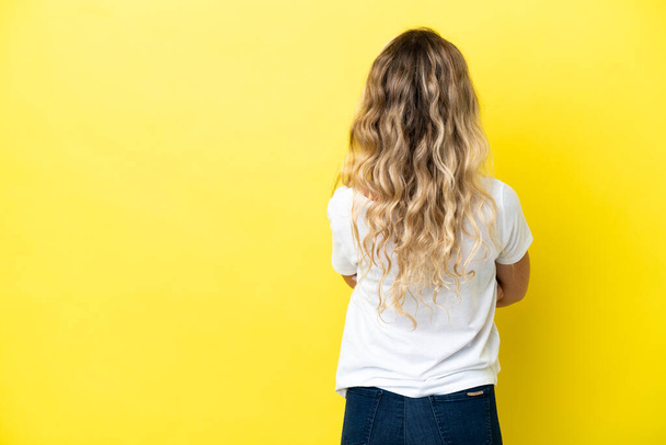 Young Brazilian woman isolated on yellow background in back position - Photo, Image