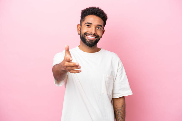 Young Brazilian man isolated on pink background shaking hands for closing a good deal - 写真・画像