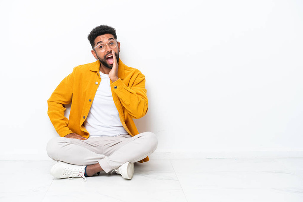 Young Brazilian man sitting on the floor isolated on white background shouting with mouth wide open - Фото, зображення