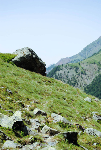 Зеленый холм, полный природы и камней в горном ландшафте с голубым и ясным небом - Фото, изображение