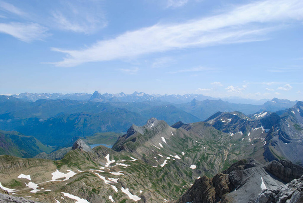 Blick vom Gipfel einer bergigen Landschaft, die die grünen Farben der Natur und den weißen Schnee der Gipfel vereint - Foto, Bild