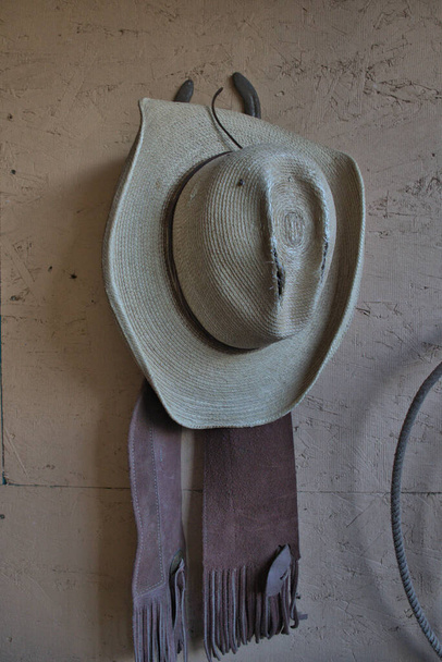 Καουμπόικο καπέλο και τύποι κρέμονται σε έναν τοίχο ράντσου. - Φωτογραφία, εικόνα