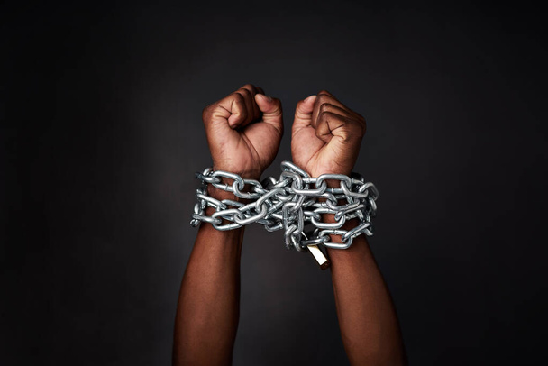 I want to break free. Cropped shot of a mans hands tied up with chains against a black background. - Foto, afbeelding