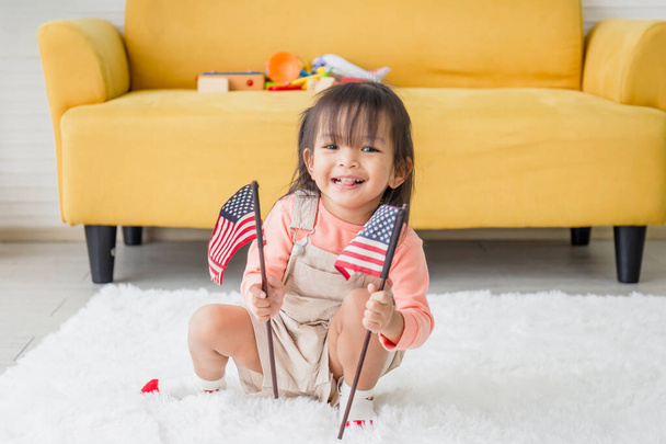 Nettes kleines Mädchen mit einer kleinen Nationalflagge der Vereinigten Staaten, kleines Mädchen spielt im Wohnzimmer - Foto, Bild
