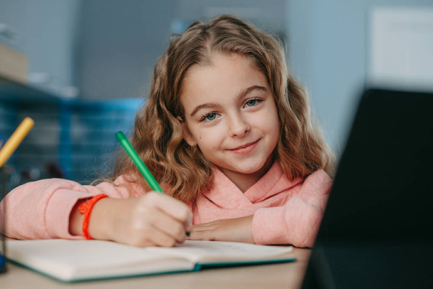 Усміхнена школярка використовує планшет для навчання, розмовляючи в веб-камері. Онлайн-освіта. Коронавська школа. Дистанційна освіта. Профілактика коронавірусу. - Фото, зображення