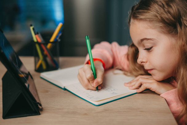 Běloška dělá domácí úkoly a studuje online s tabletem za stolem. Dítě studující z domova. Domácí výuka během karantény a vypuknutí koronaviru. e - Fotografie, Obrázek