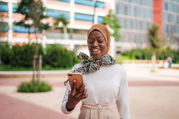 Sonriente dama musulmana negra comprobando el mensaje en el teléfono inteligente - Foto, Imagen