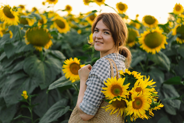 Krásná mladá žena se slunečnice těší přírodě a směje se na letním slunečnicovém poli. - Fotografie, Obrázek