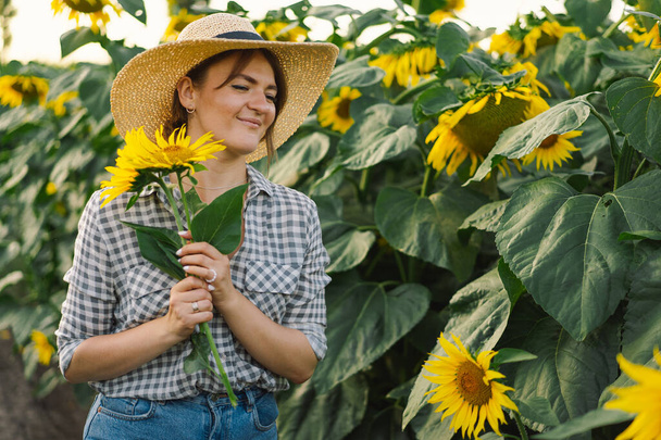 Piękna młoda kobieta ze słonecznikami ciesząca się naturą i śmiejąca się na letnim polu słonecznika. - Zdjęcie, obraz