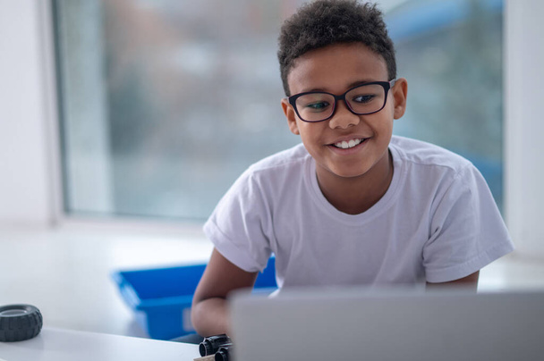 A smiling dark-skinned boy sitting at the laptop - Φωτογραφία, εικόνα