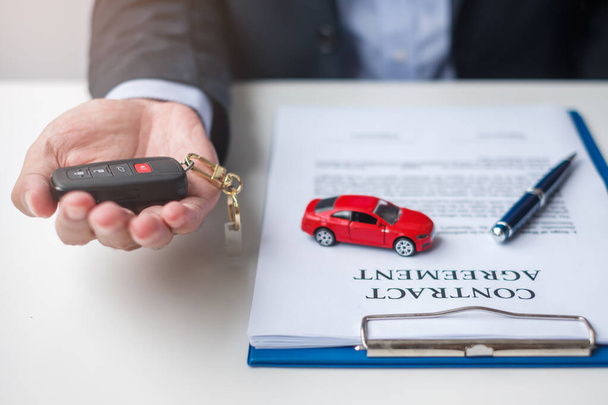 Businessman hand holding remote keyless with car toy, pen and contract document. buy and sale, insurance, rental and contract agreement concepts - Photo, Image