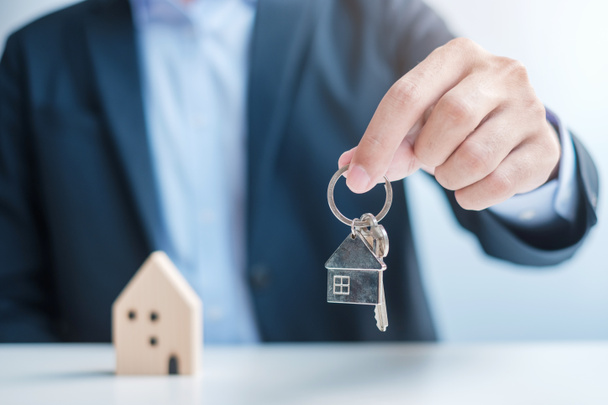 Podnikatel drží klíč s dřevěným modelem Home. Nemovitosti, koupě a prodej, Pojištění nemovitostí, pronájem a smlouvy - Fotografie, Obrázek