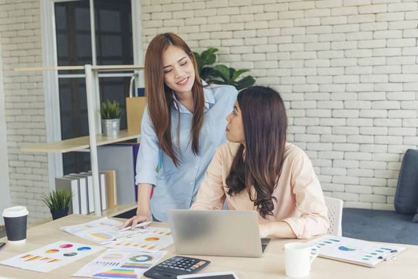 Zwei asiatische Freiberuflerinnen lesen Finanzdiagramme und analysieren Marketingdaten. Asiaten arbeiten im Büro. Zwei Geschäftsfrauen treffen sich mit Laptop am Schreibtisch. - Foto, Bild