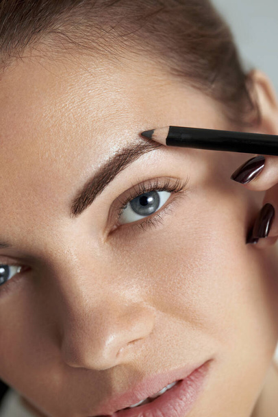 Eyebrow makeup. Beauty model shaping brows with brow pencil closeup. Beautiful sexy woman with eyebrows correction. - Fotó, kép
