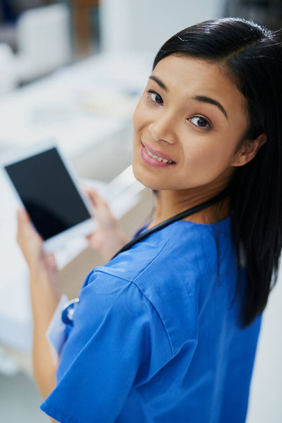 Its the only assistant I need. High angle portrait of an attractive young female nurse using a tablet while standing in the hospital. - Fotoğraf, Görsel