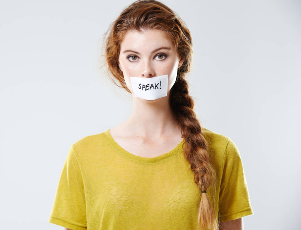 Usa la tua voce. Ritratto in studio ritagliato di una giovane donna con un'etichetta che dice di parlare coprendo la sua bocca. - Foto, immagini