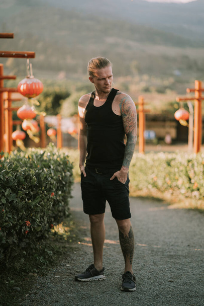 Tattooed man is standing on a trail with Chinese lanterns at viewpoint in Pat Thailand - Foto, imagen
