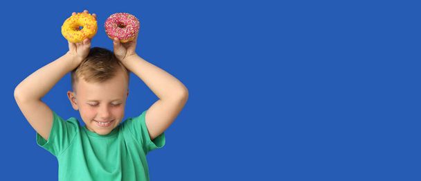 Funny little boy holding donuts on blue background with space for text - Photo, Image