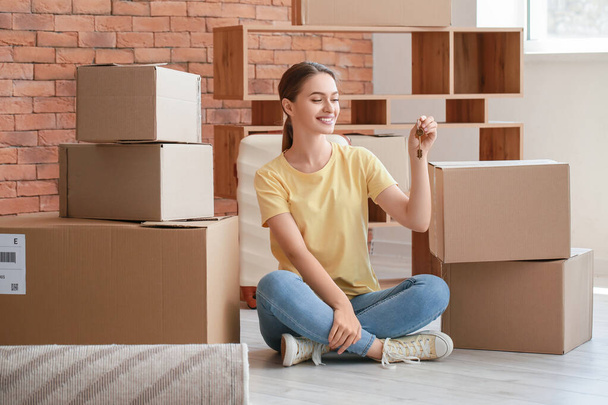 Mujer joven y feliz con llave sentada en el suelo en su nuevo apartamento - Foto, Imagen