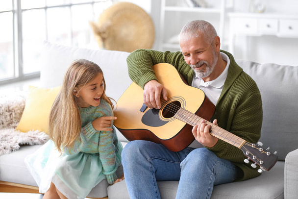 Älterer Mann mit seiner kleinen Enkelin, die zu Hause Gitarre spielt - Foto, Bild