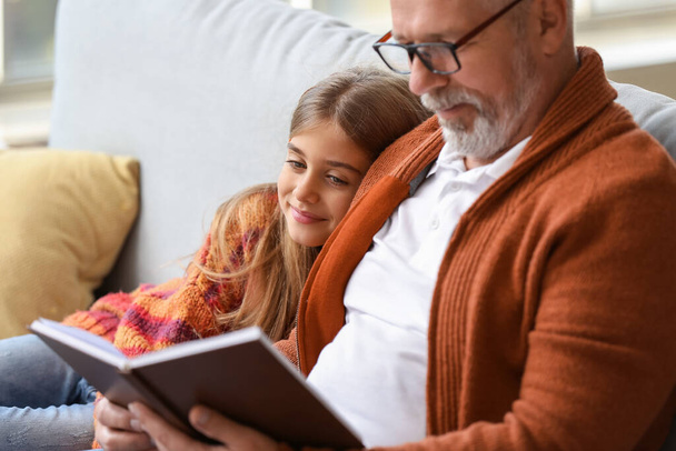 Pieni tyttö isoisänsä kanssa lukemassa kirjaa kotona - Valokuva, kuva
