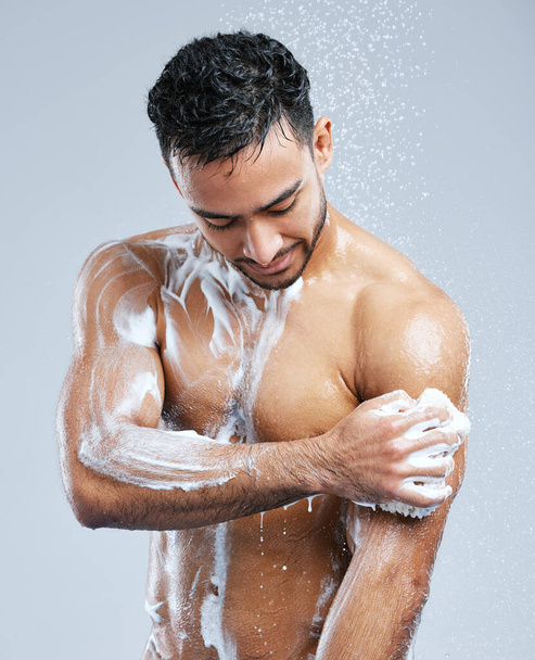 Acércate y frota. Estudio de un joven guapo tomando una ducha sobre un fondo gris. - Foto, imagen