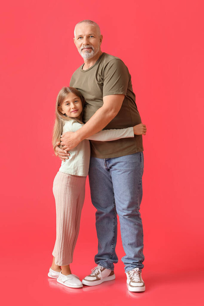 Маленька дівчинка з дідом обіймається на червоному тлі
 - Фото, зображення