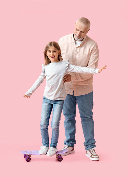 Маленькая девочка со скейтбордом и ее дедушка на розовом фоне - Фото, изображение
