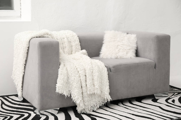 Szürke kanapé fehér takaróval és párnával a világos fal mellett - Fotó, kép