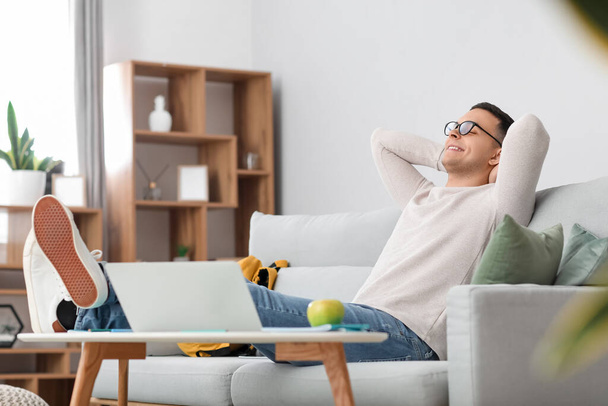 Студент-мужчина отдыхает дома на диване - Фото, изображение