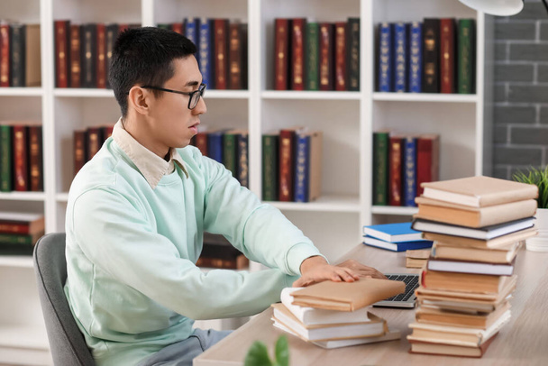 Студент-азиат за столом в библиотеке - Фото, изображение