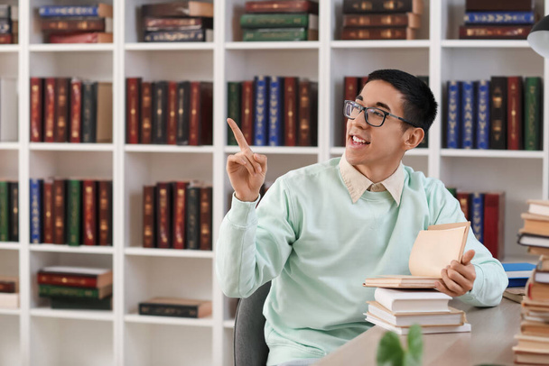 Homme asiatique étudiant avec des livres pointant vers quelque chose dans la bibliothèque - Photo, image