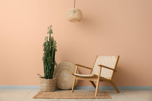 Большой кактус с пуфом и креслом возле бежевой стены - Фото, изображение