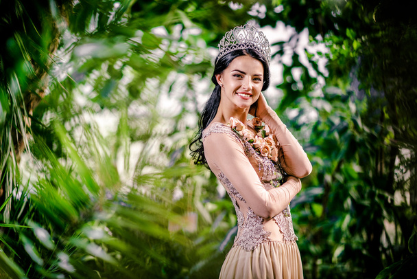 Elegant smiling lady with tiara on a head posing in a forest - Фото, зображення