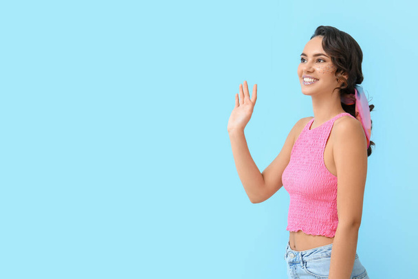 Attraente giovane donna con brillantini sul viso agitando la mano contro lo sfondo blu - Foto, immagini