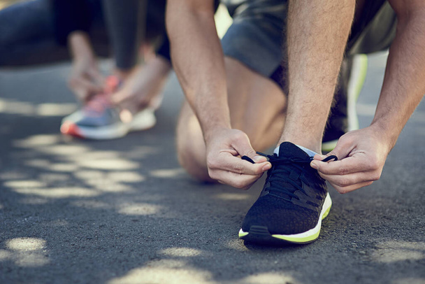 Making sure its nice and tight. Cropped shot of two unrecognizable people tying their laces before a run. - 写真・画像