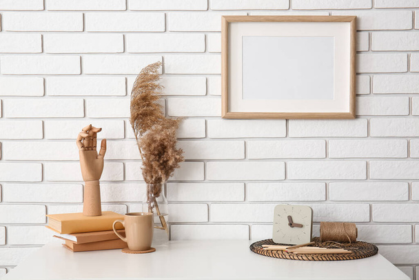 Робоче місце з дерев'яною рукою, книгами, чашкою, травою пампушок у вазі та годинником біля білої цегляної стіни
 - Фото, зображення