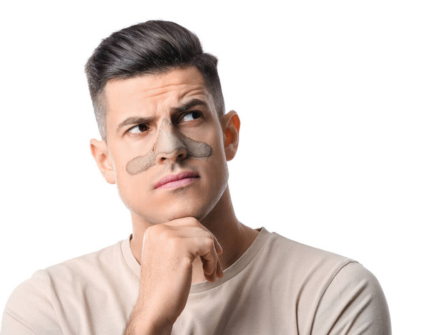 Thoughtful young man with applied clay mask on white background - Photo, Image