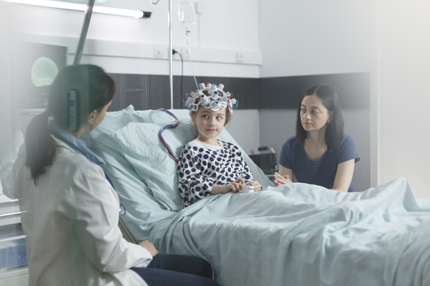 Lastenklinikan asiantuntija tarkistamassa EEG-kuvauksen tuloksia sairaasta tytöstä lastenosastolla. - Valokuva, kuva